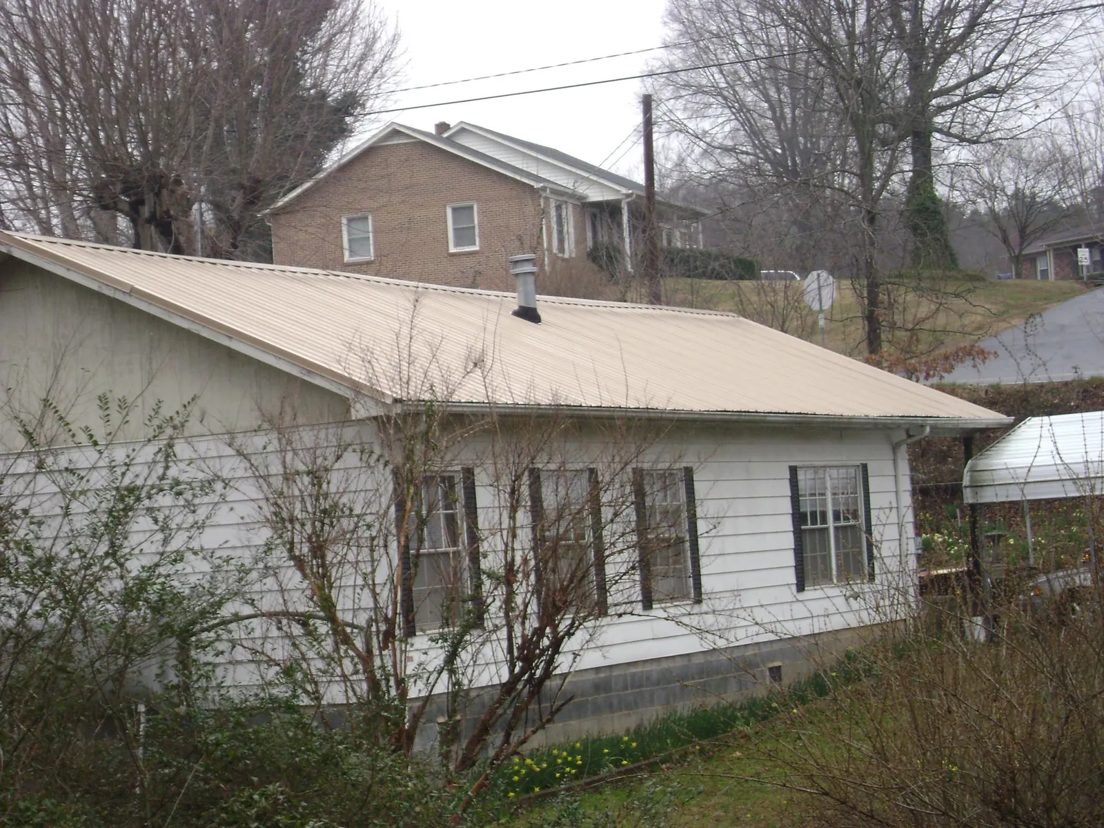 Tan metal roof on a white sided house set into a hillside — Commercial Roofing by Roofing Brothers in Hammond